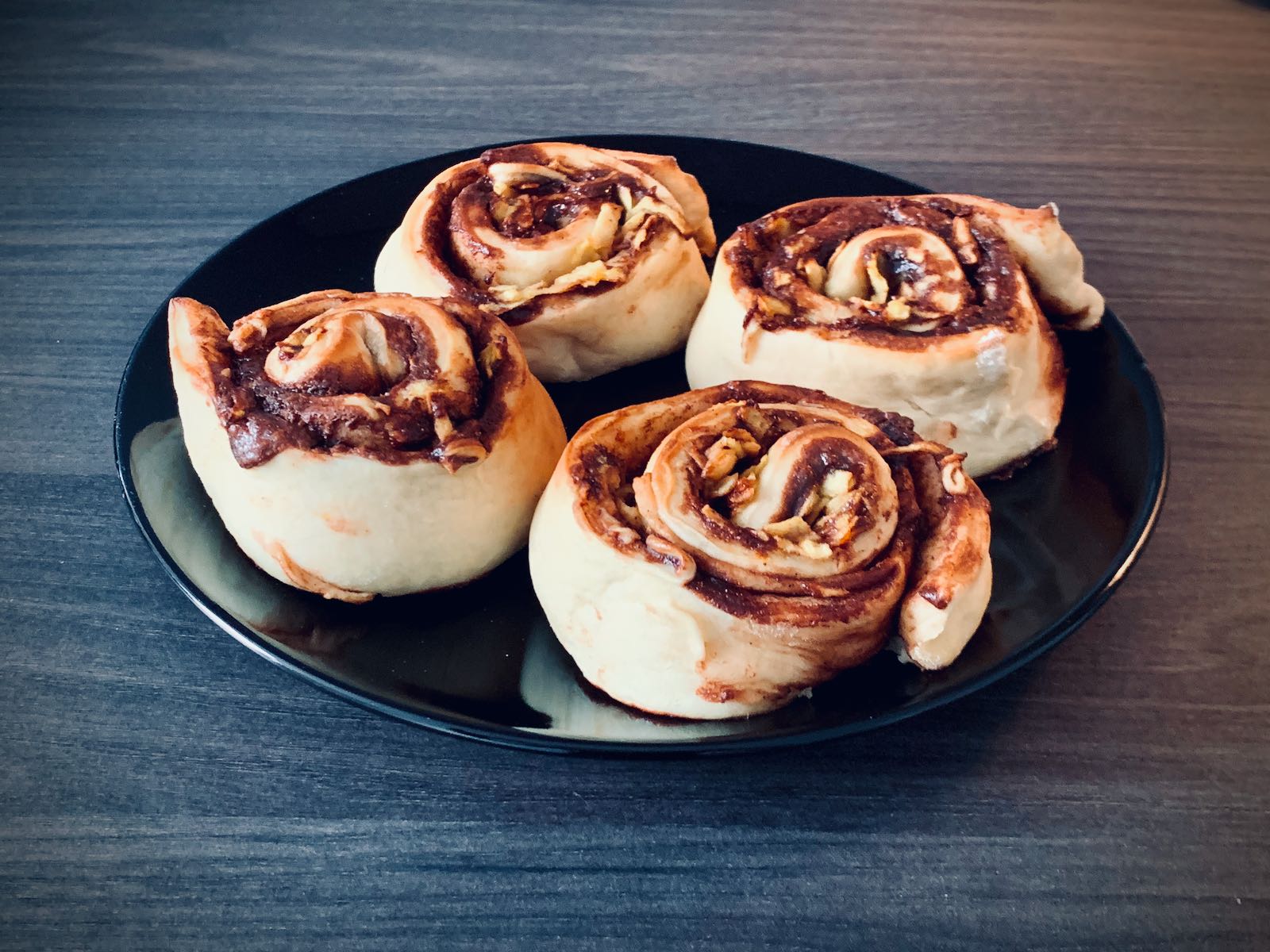 Photo of 4 cinnamon rolls filled with chocolate and grated apple on a black plate