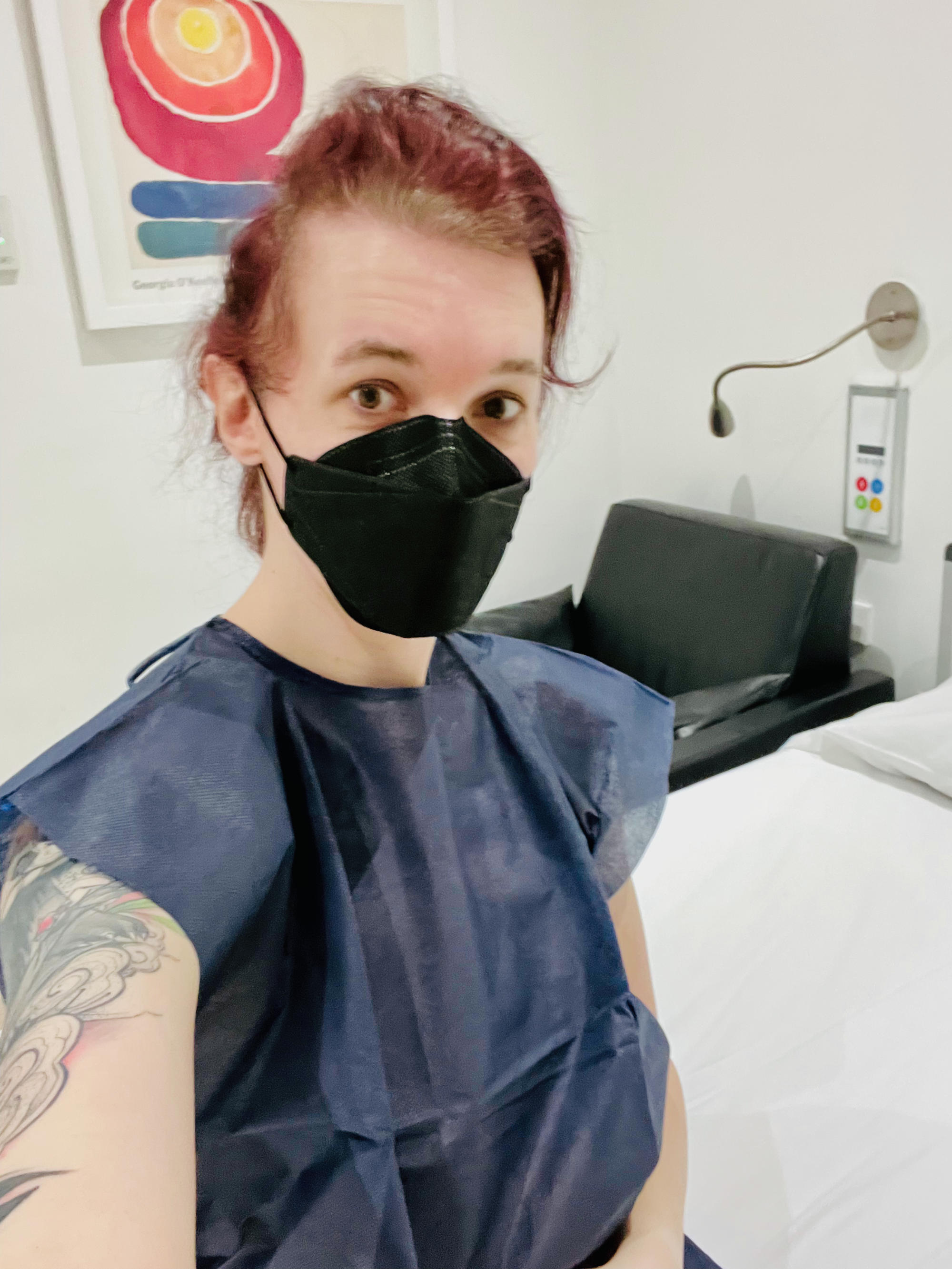 selfie wearing a hospital gown, messed up hair and a face mask
