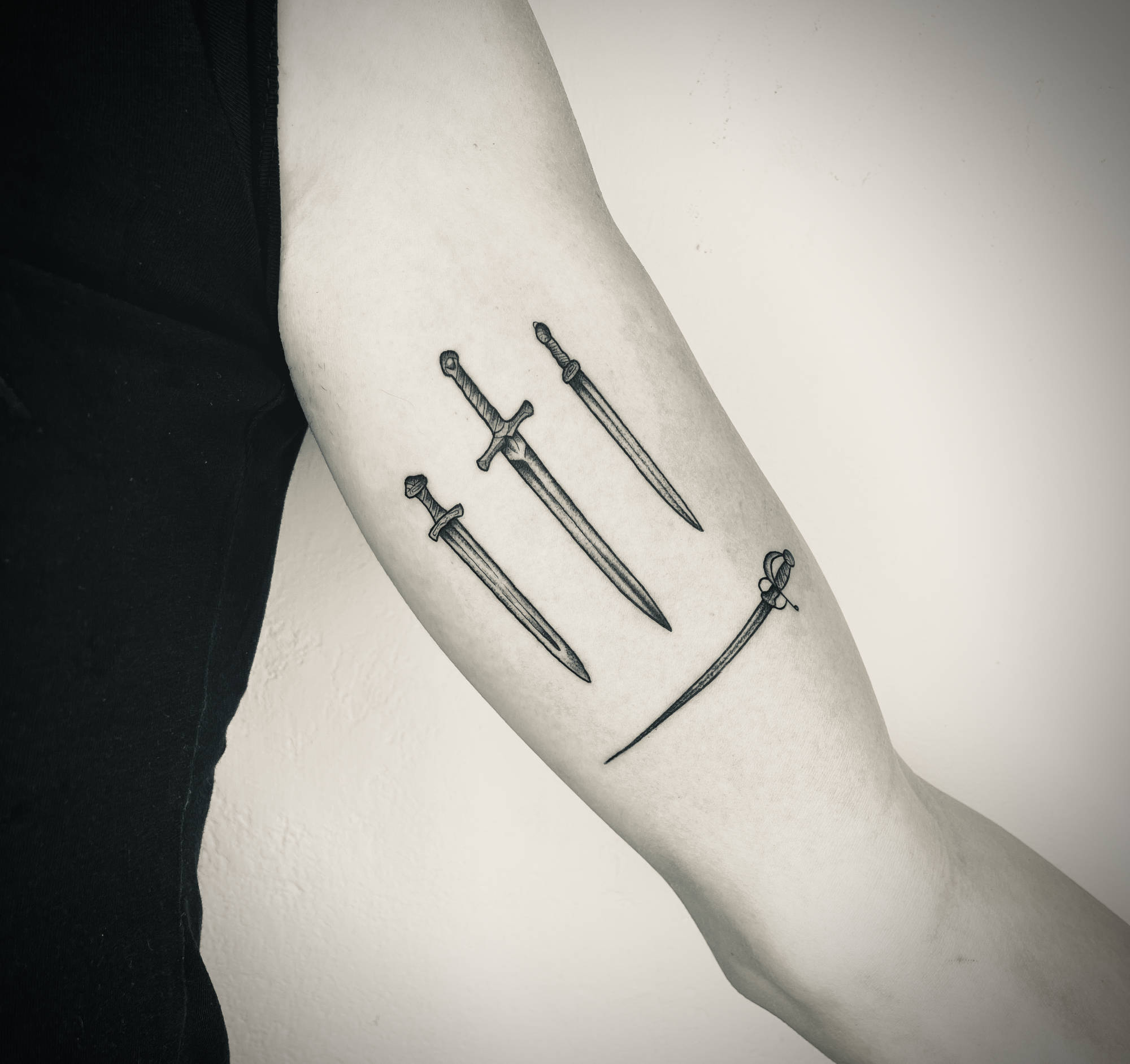 Upper arm with a tattoo of four swords