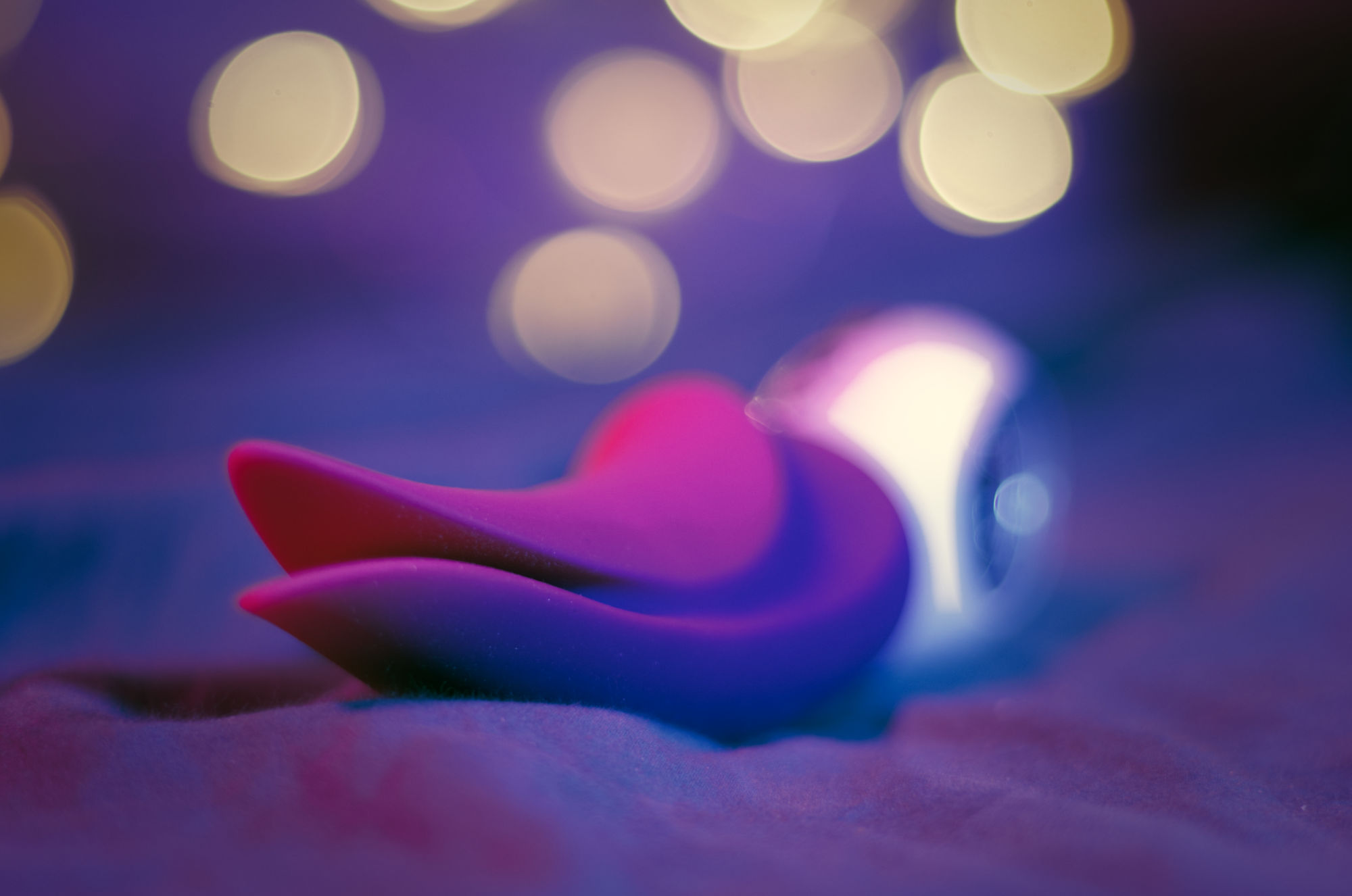 Front view of the Volta, a purple vibrator with a tapered silicone body that ends in a spit tongue-like pieces. Very blurry background with purple/blue lighting and christmas lights