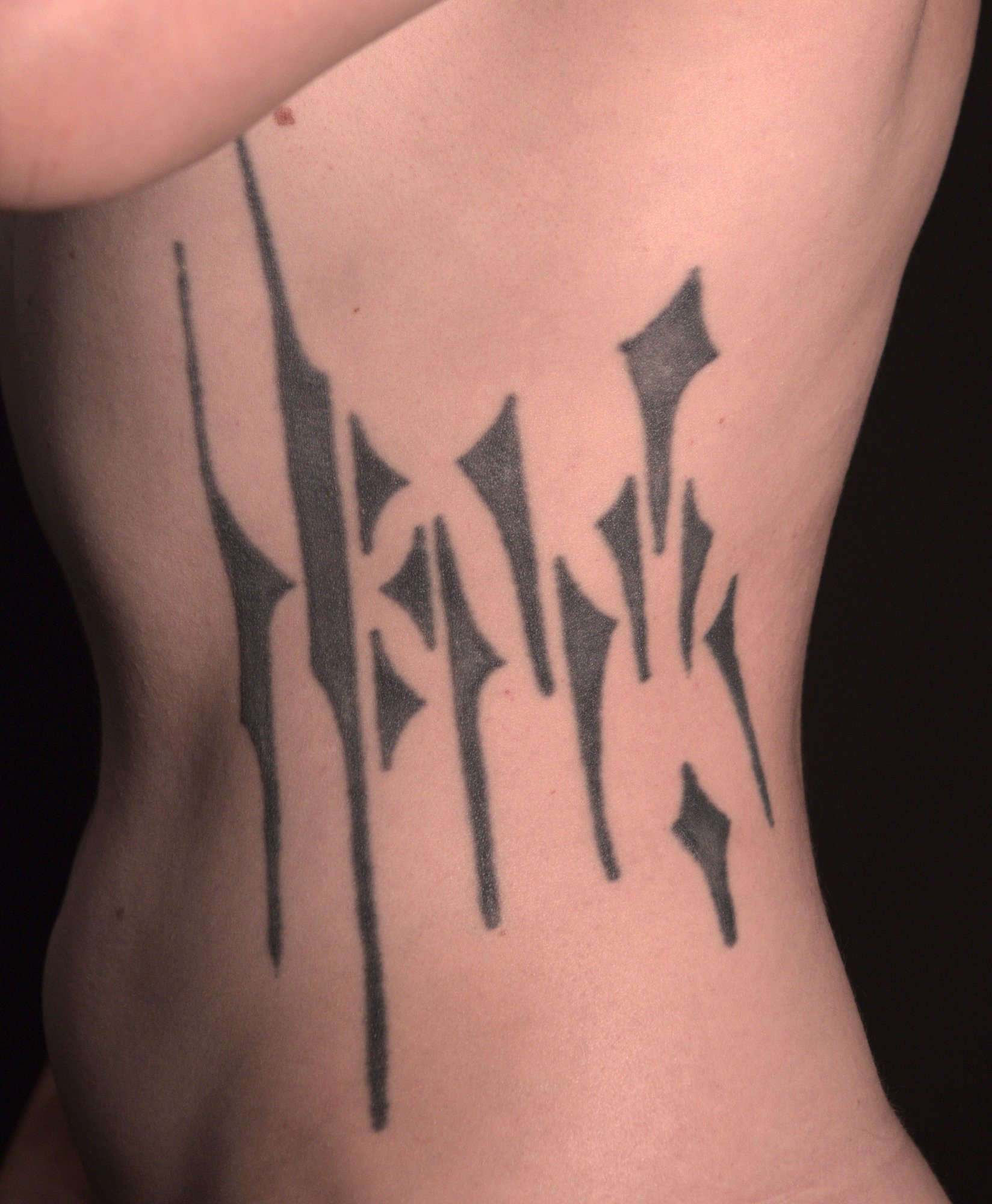 An abstract black tattoo made from pointy shapes, on the left side of the torso from hips to chest