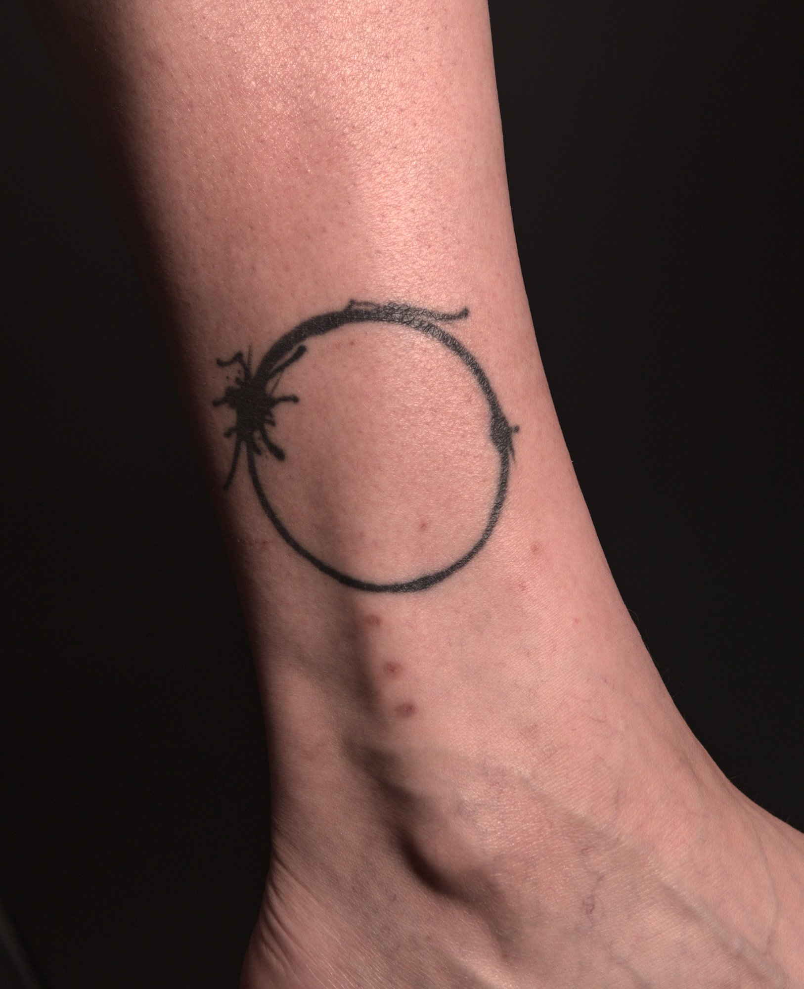 tattoo of the heptapod glyph for 'human' from the movie Arrival: a black ring with ink blotches