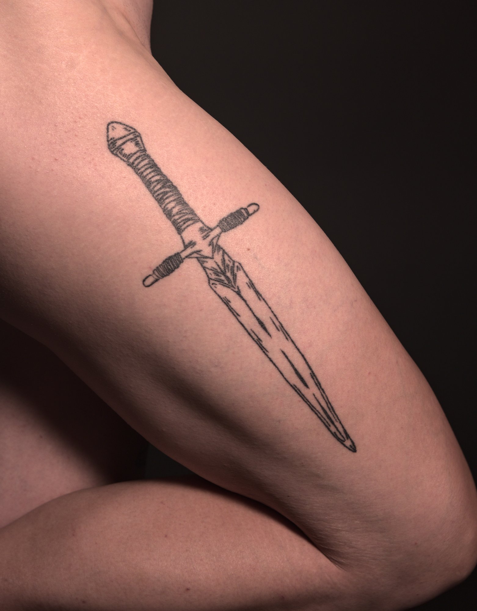 tattoo of a large and roughly shaped dagger on the outside right thigh