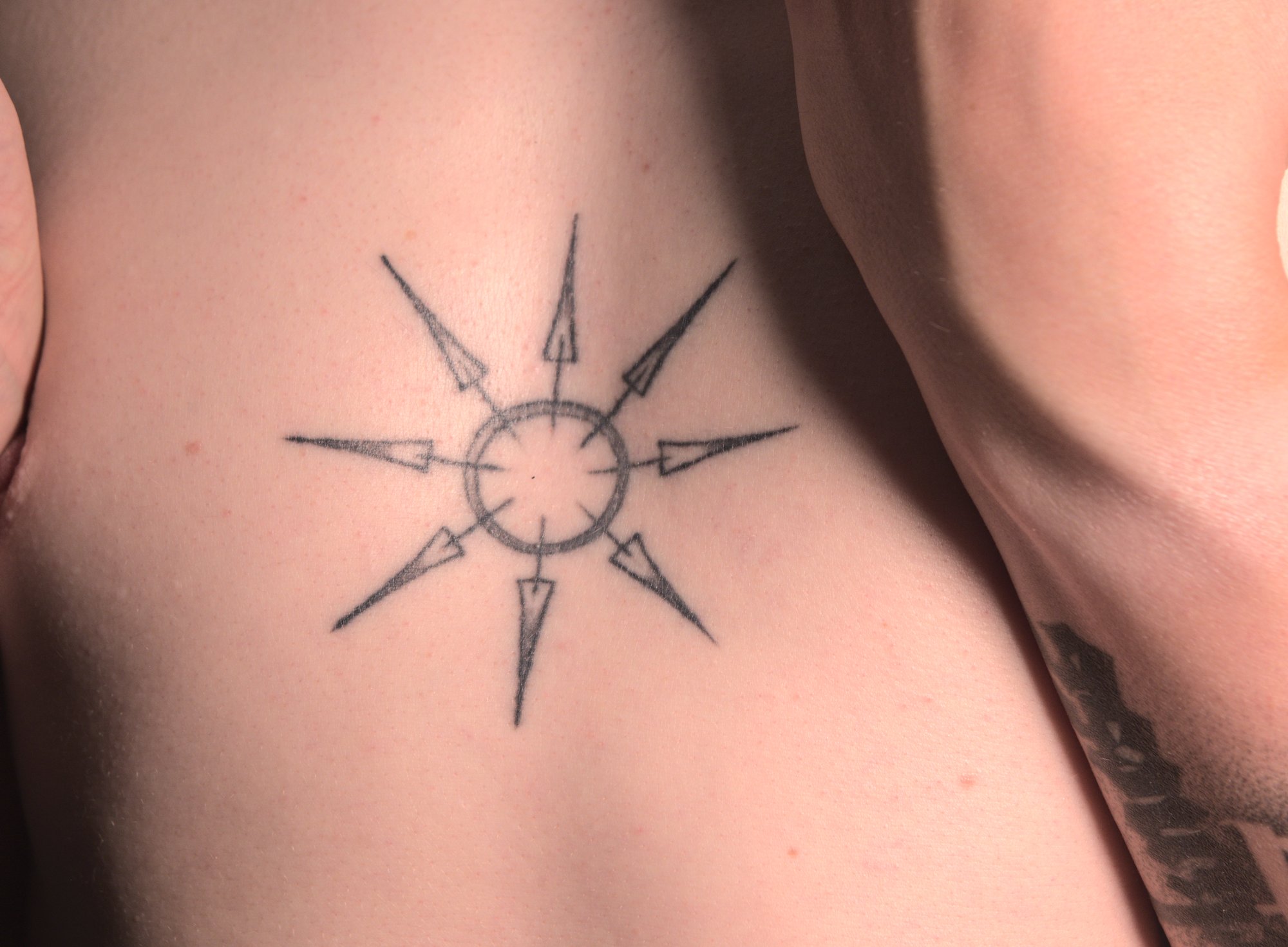 tattoo of an eight-pointed star in the center of the chest, made from a ring and thin arrows