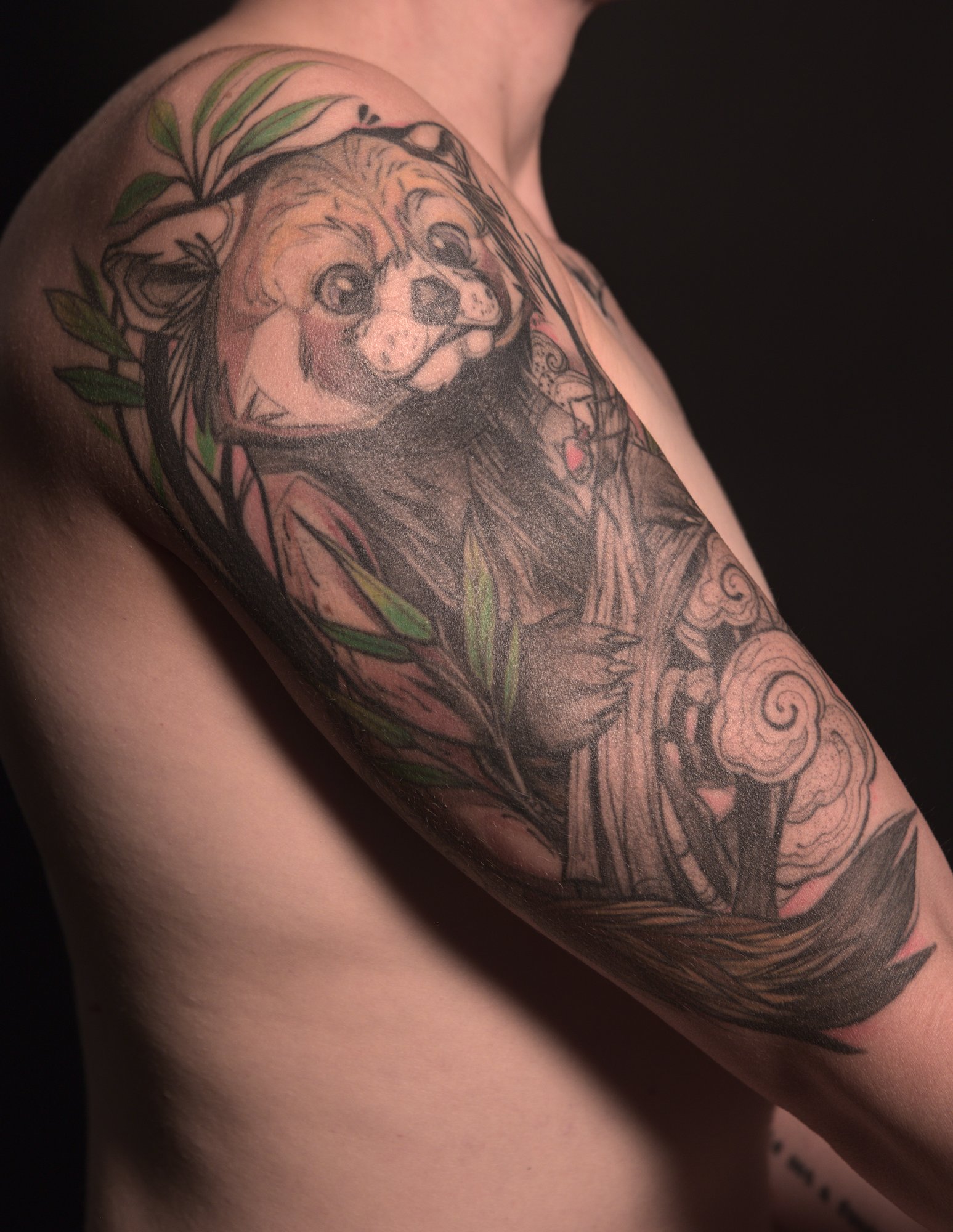 upper arm tattoo of a red panda between leaves and clouds, looking at a small red bug on a tree branch