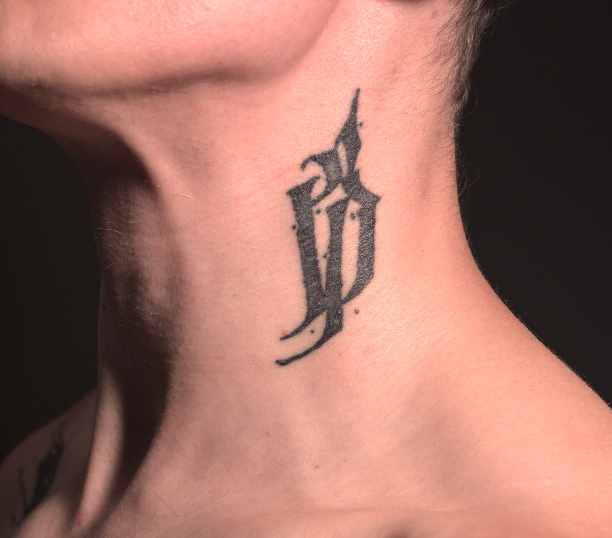tattoo of an abstract blackletter glyph on the left side of the neck